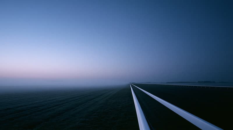 Empty racecourse straight at dawn, white running rail in the foreground